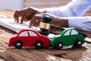 Car Accident Lawyer Morgantown, WV with two wooden toy cars with judge gavel and person typing on computer keyboard