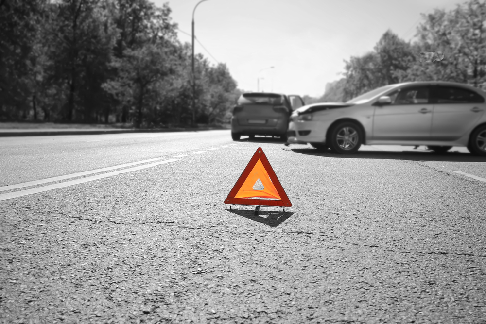 Emergency Car Kit: Essential Items To Include - Hazard warning triangle laid out on the road behind two crashed cars, black and white photo with a red accent on a triangle